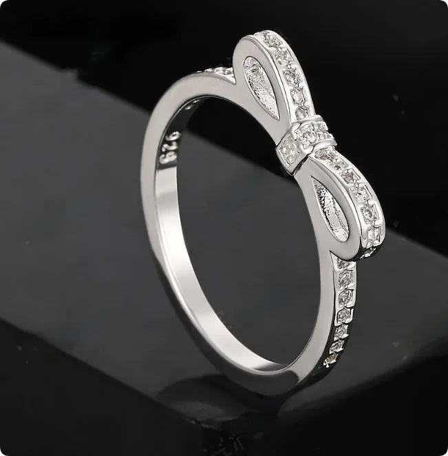 Silver coloured bow-shaped ring with zircon crystal details on a white background.