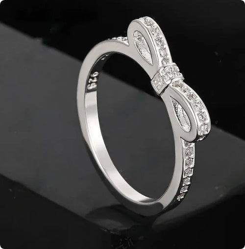 Silver coloured bow-shaped ring with zircon crystal details on a white background.