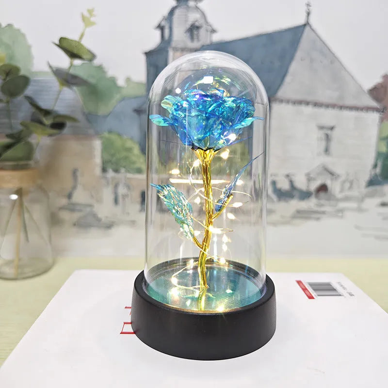 Small decorative table lamp with coloured LED lights illuminating plastic flowers under a glass dome.