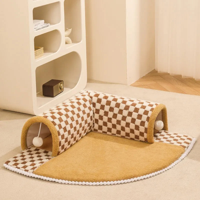 Brown plaid collapsible cat tunnel bed with a central mat on a wooden floor.