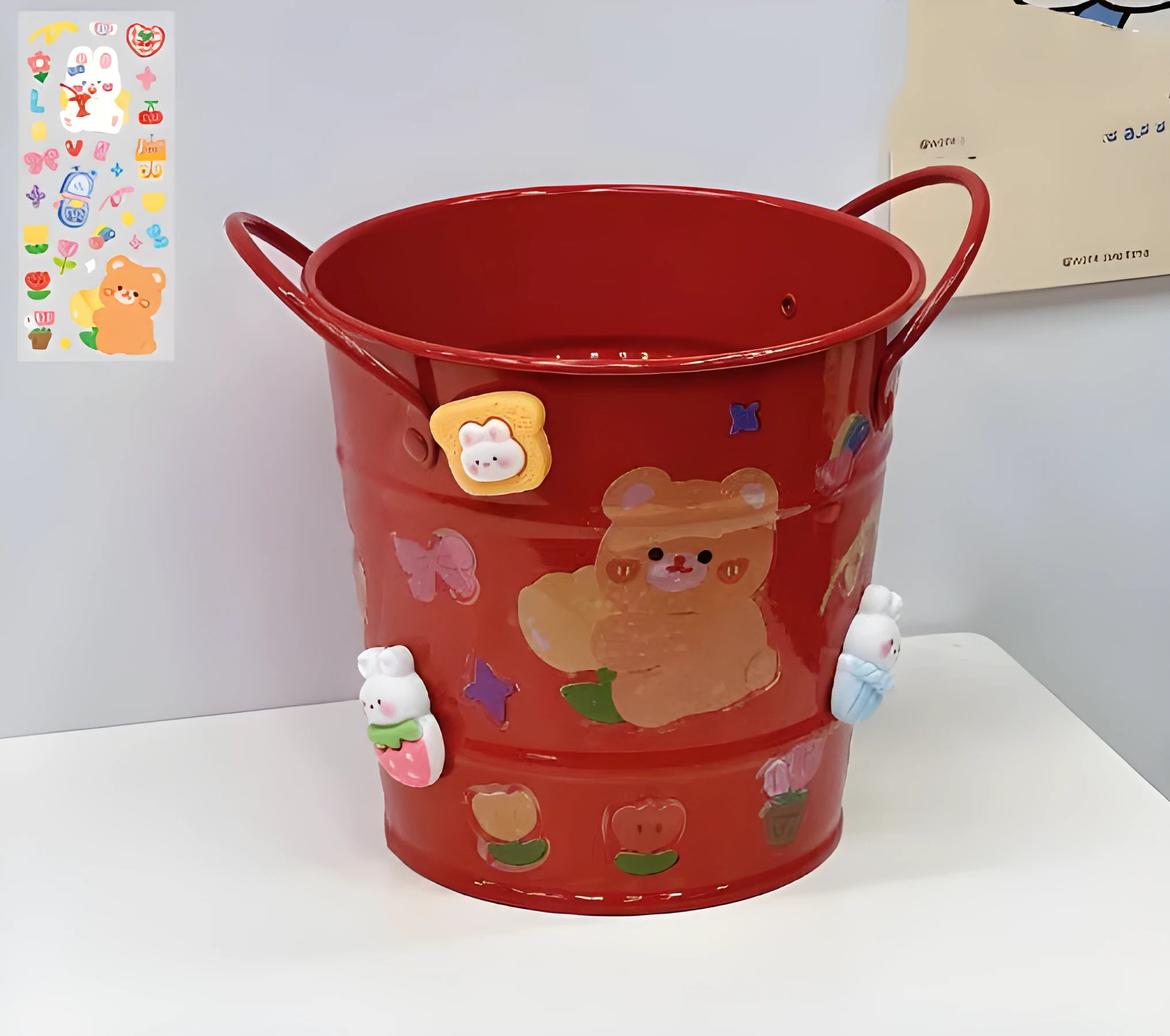 Round metal pen holder in a choice of colours including pink, green, red, white and yellow on a desk.