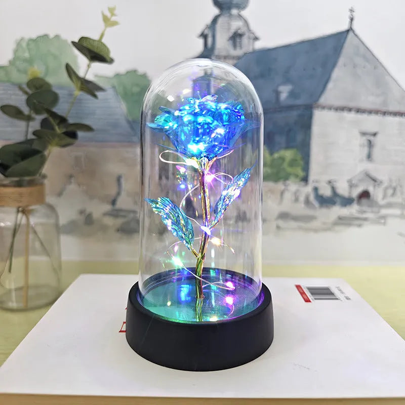 Small decorative table lamp with coloured LED lights illuminating plastic flowers under a glass dome.