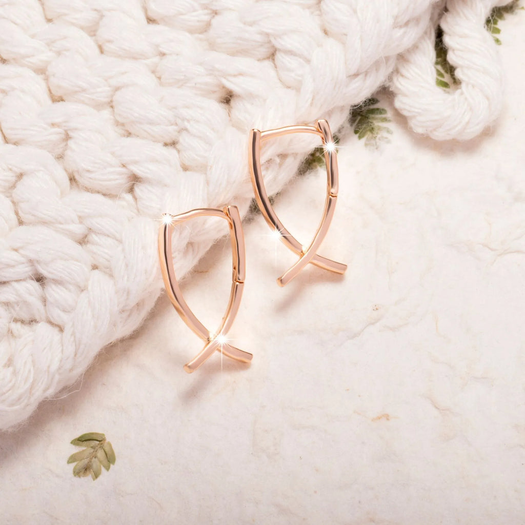 A pair of rose gold coloured cross shaped earrings on a plain background.