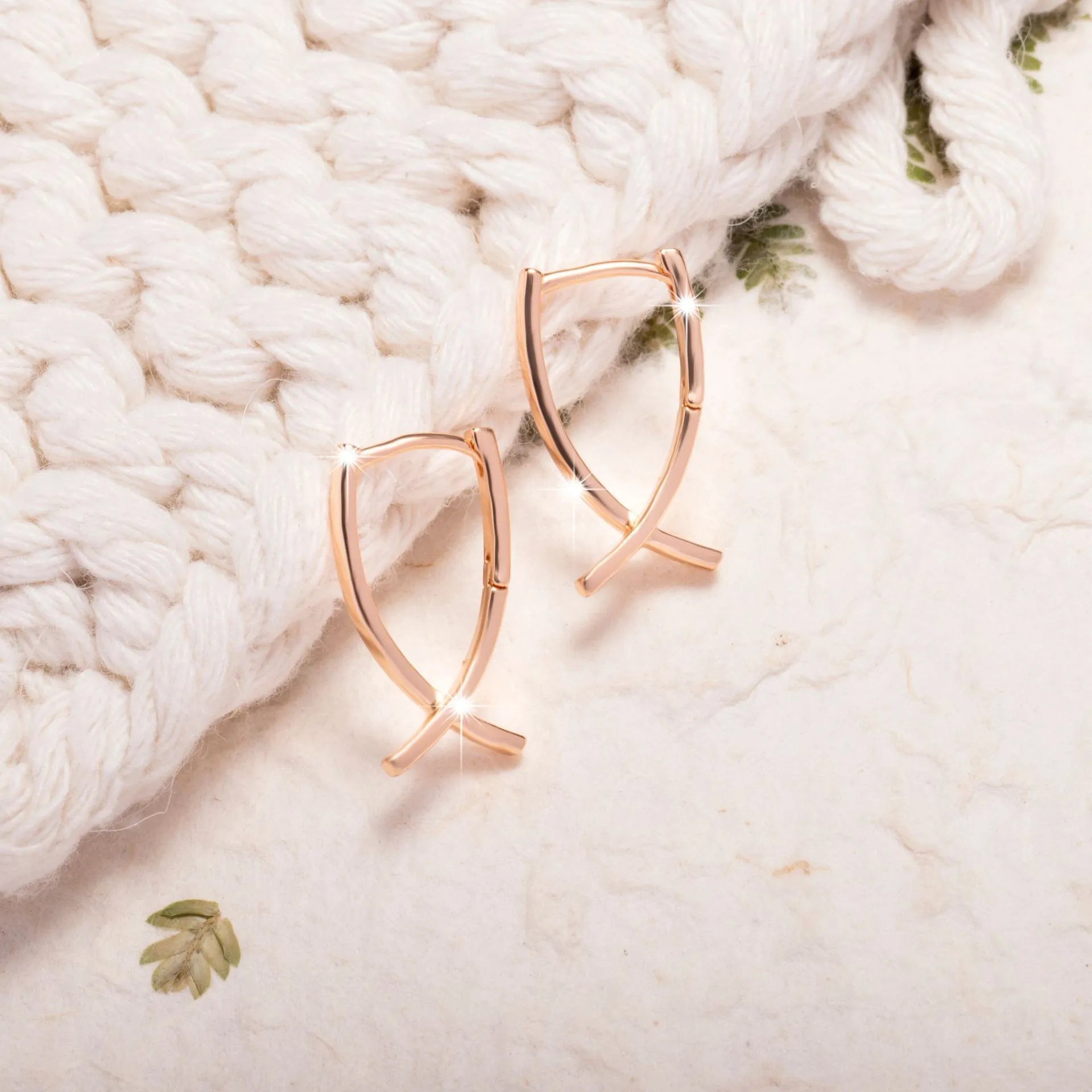A pair of rose gold coloured cross shaped earrings on a plain background.