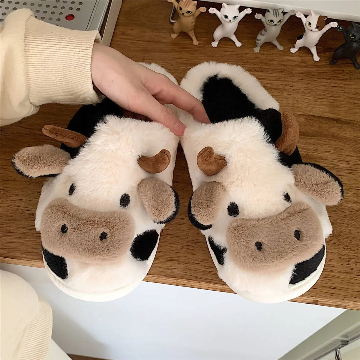 White cartoon cow plush house slippers for women with a non-slip textured sole.
