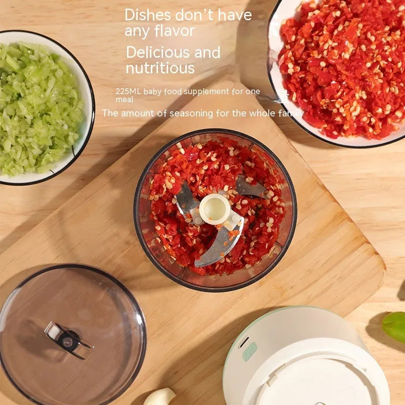 Mini electric food processor in light green with transparent cup and stainless steel blades on countertop.