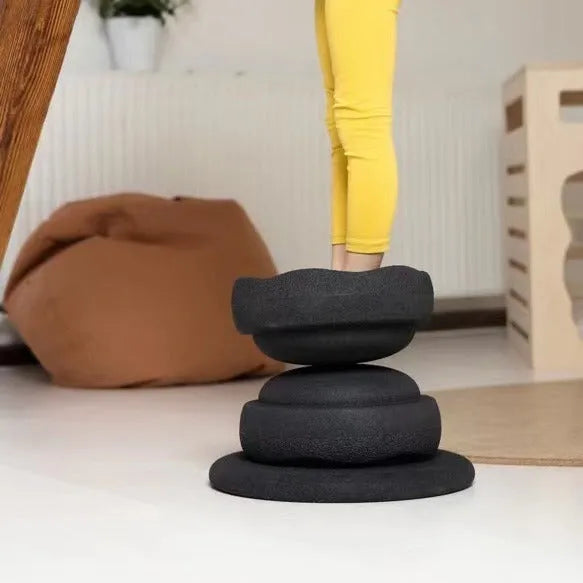 Plastic surfboard-shaped balance board for children, shown in mixed wood colour and black options.