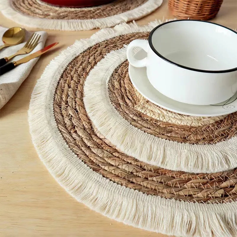 Round natural papyrus placemat with tassel trim on a wooden table.