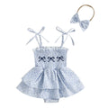 Baby girl wearing cotton blend floral triangle jumpsuit with suspenders and matching headscarf, sitting on a light background