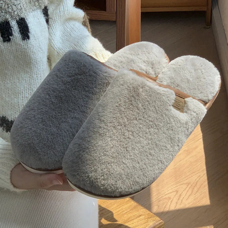 Pair of solid colour plush house slippers with PVC sole on a wooden floor.