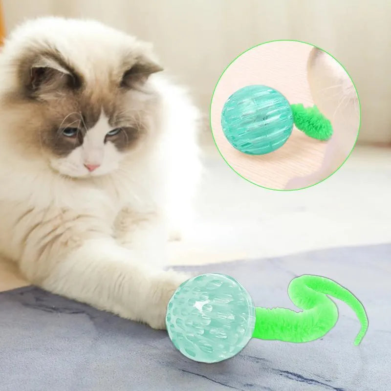 Green TPR bouncy ball with pink plush worm tail cat toy on floor