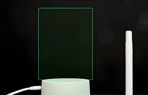 Black 3D LED handwritten acrylic message board with remote control on a desk.