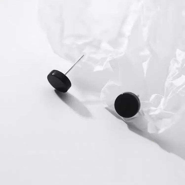 A pair of simple geometric round S999 Sterling Silver flat bone stud earrings in silver and black, showing size variation.