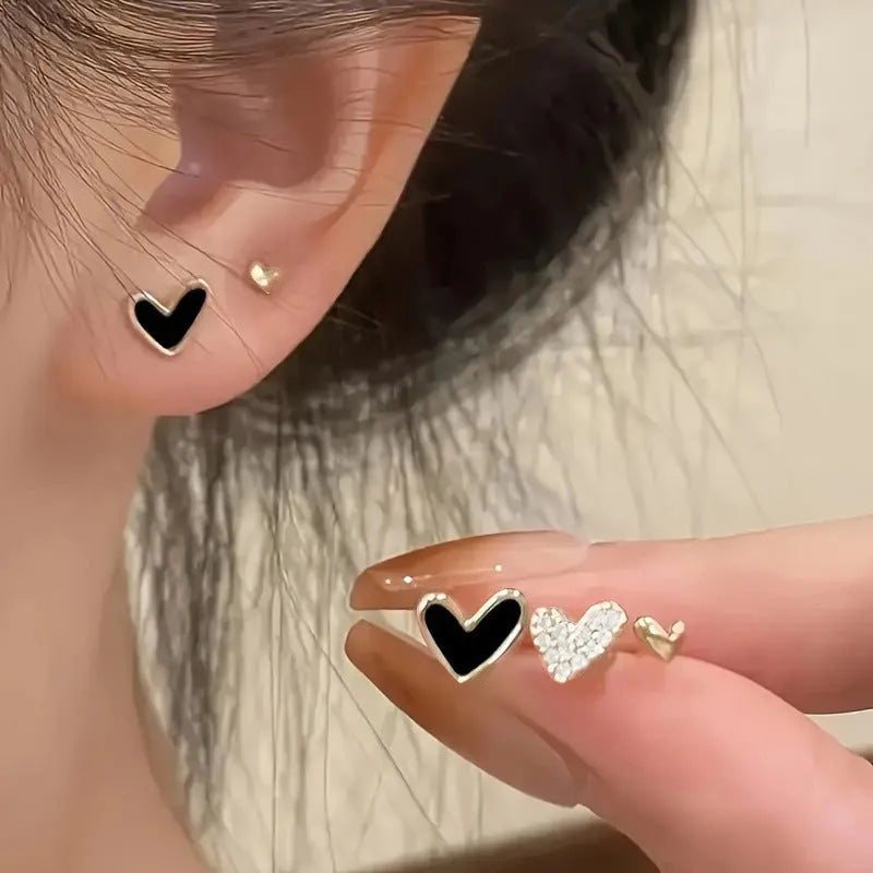 Three pairs of women's heart-shaped alloy earrings in gold, black, white, and pink colours
