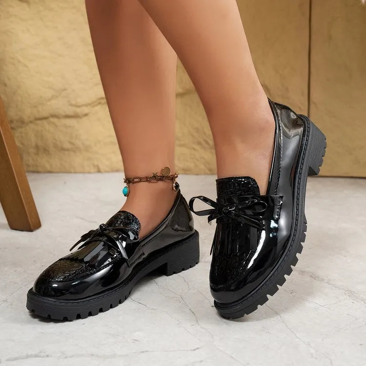 Brown women's slip-on loafers with a black bow detail on the front.