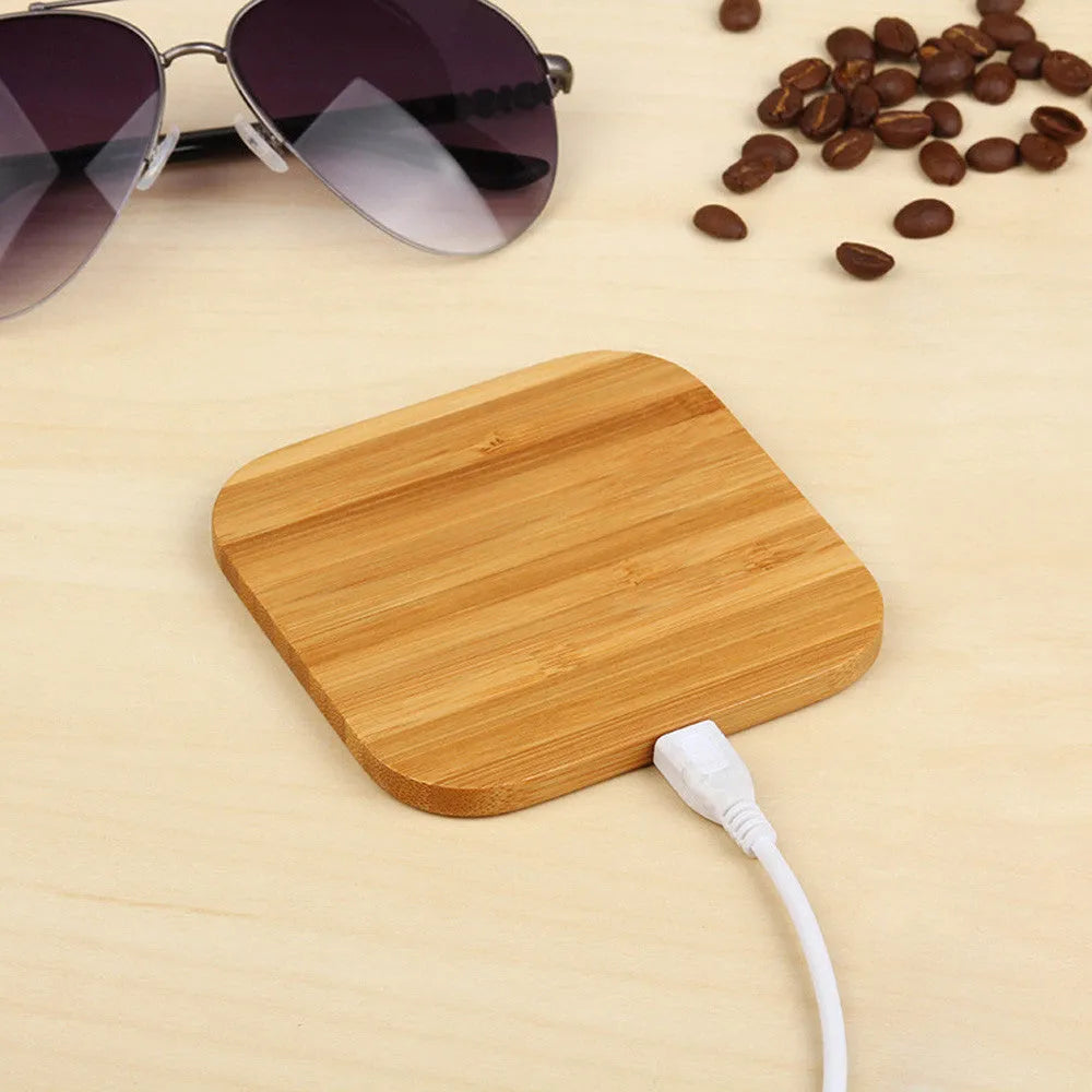 Square wooden bamboo 5W Qi wireless charging pad on a desk next to a smartphone.