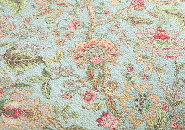 Blue cotton quilted bedspread with detailed floral and bird pattern, shown on a bed.