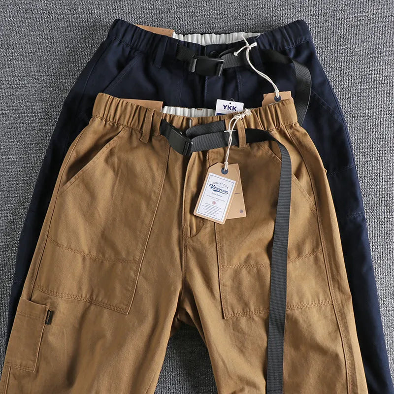 Men's khaki cotton work trousers with a black buckle belt and zip fly closure.
