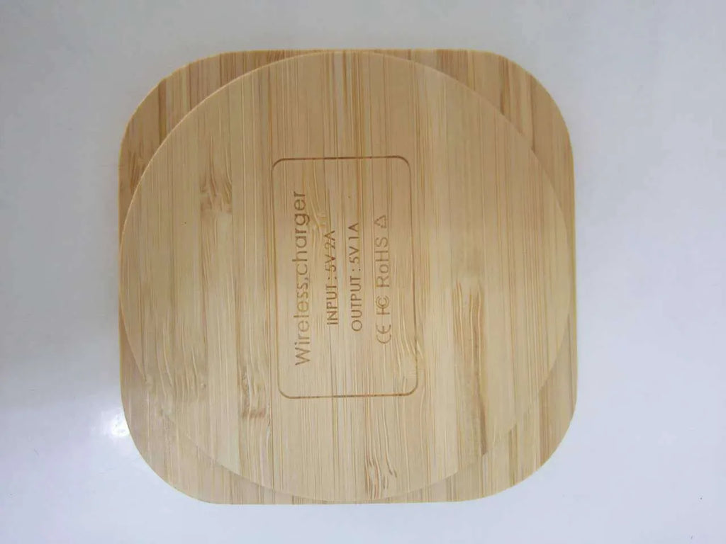 Square wooden bamboo 5W Qi wireless charging pad on a desk next to a smartphone.