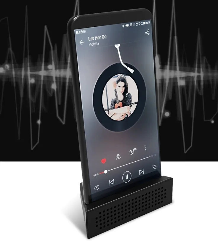 A small, coloured plastic phone amplifier holder holding a mobile phone on a desk.