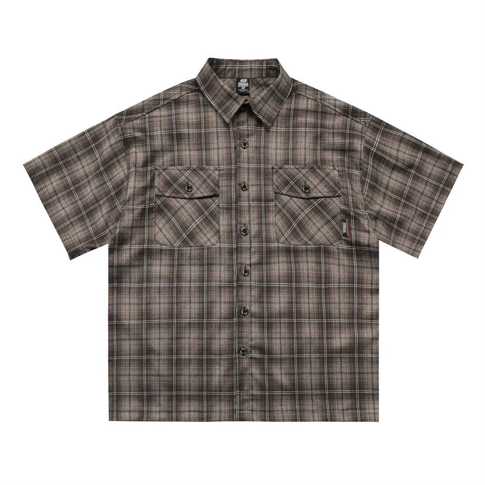 Man wearing a black and brown plaid short sleeve shirt with embroidered letter on lapel