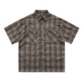 Man wearing a black and brown plaid short sleeve shirt with embroidered letter on lapel