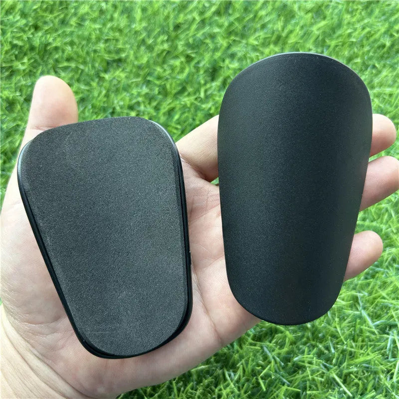 Extra small black and white plastic football shin guards for youth players, size 8cm by 5cm.