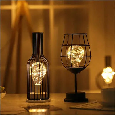 Minimalist hollow iron table lamp in red wine glass style on a wooden desk.