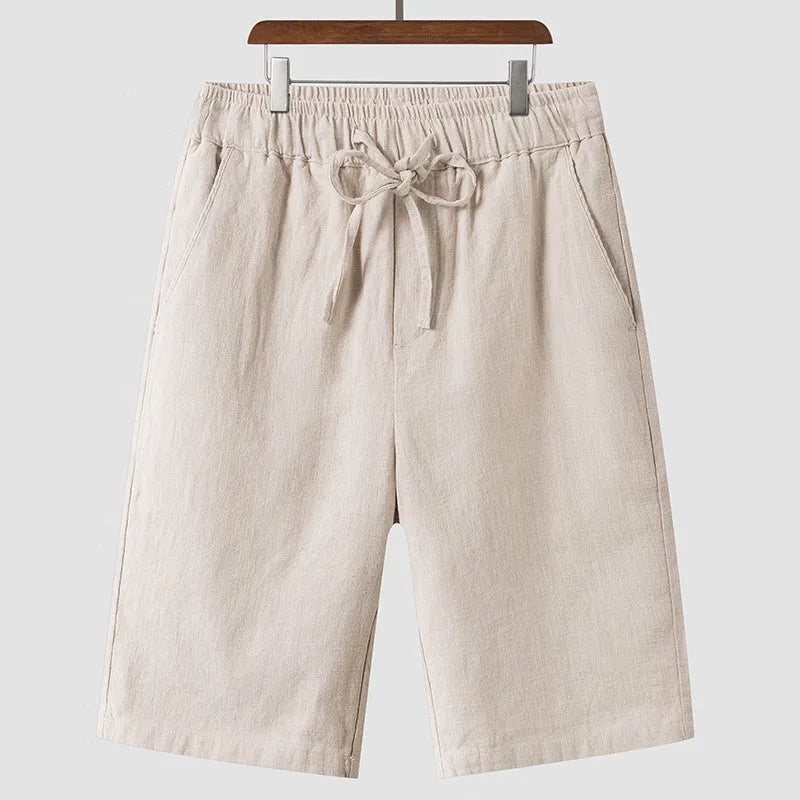 Men's beige linen casual shorts with a loose fit and cropped length on a plain background.