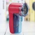 White handheld electric lint remover for clothing on a grey background showing its compact size.