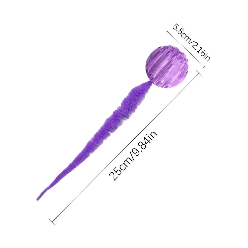 Green TPR bouncy ball with pink plush worm tail cat toy on floor