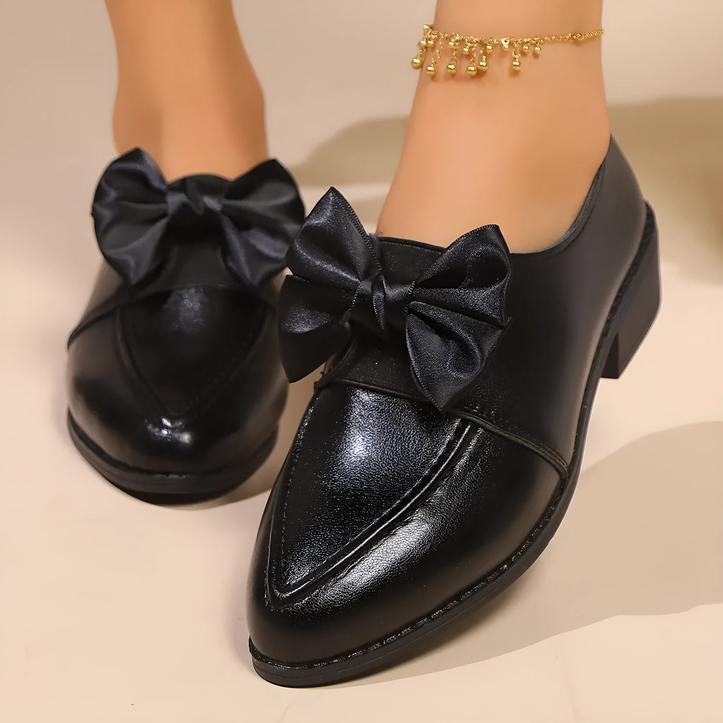 Women's British-style leather-look shoes with decorative bow detail on pointed toe