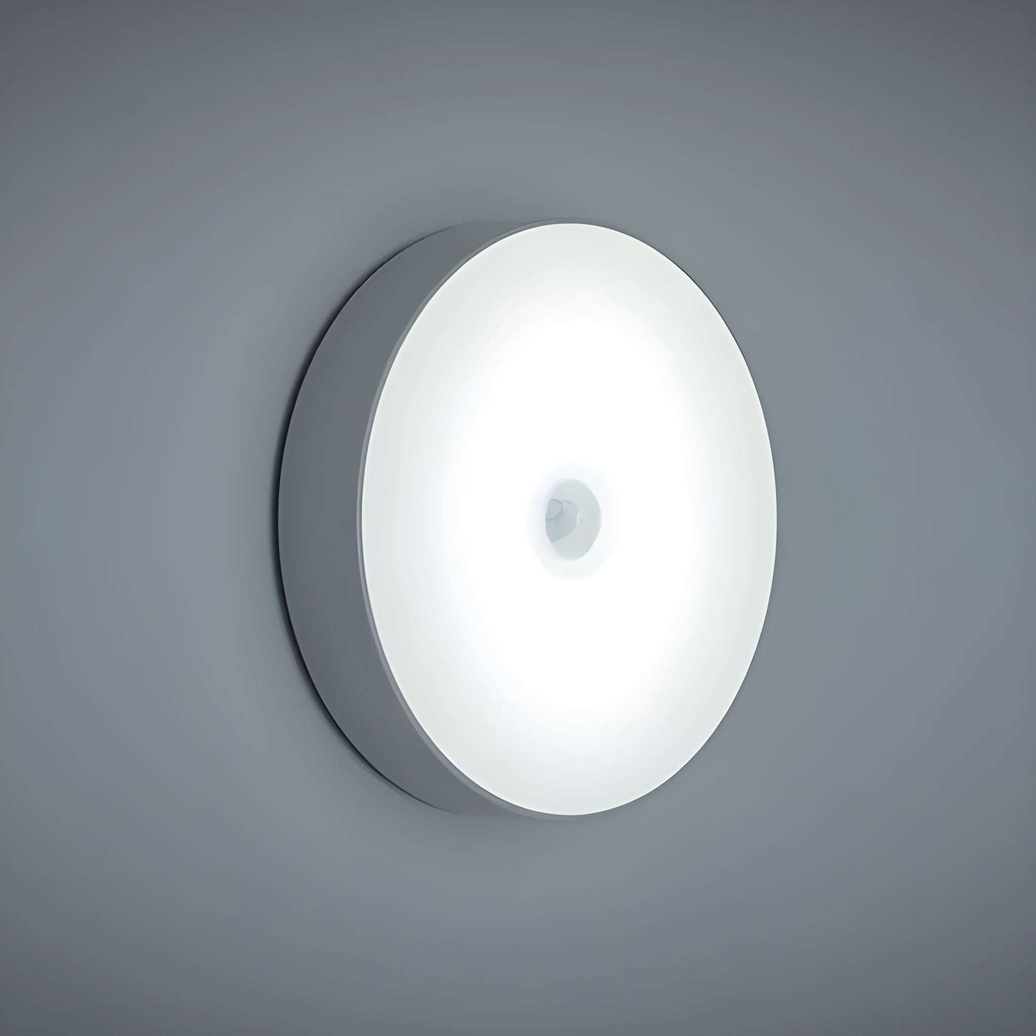 Small white circular motion sensing LED night light with adhesive backing next to a USB charging cable.