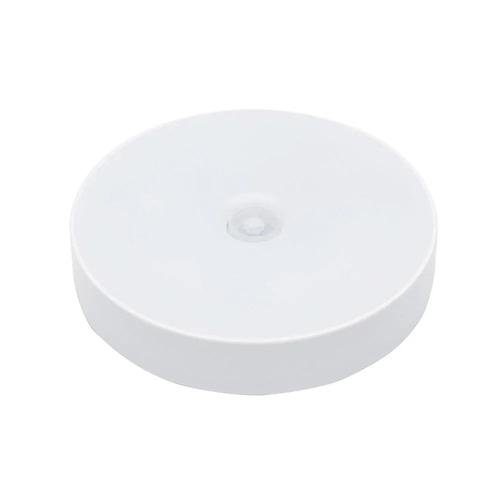 Small white circular motion sensing LED night light with adhesive backing next to a USB charging cable.