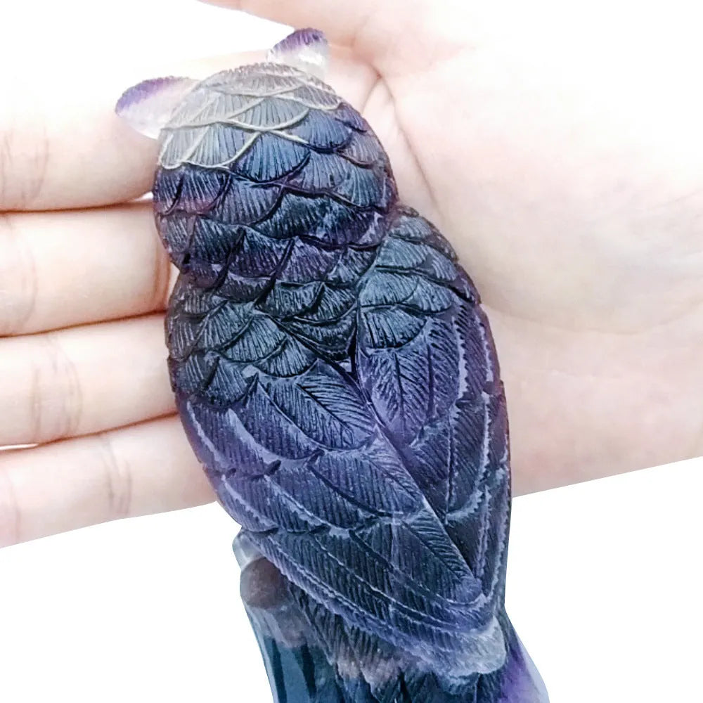 Hand-carved purple fluorite owl ornament on a neutral background, showing natural stone colour and texture.