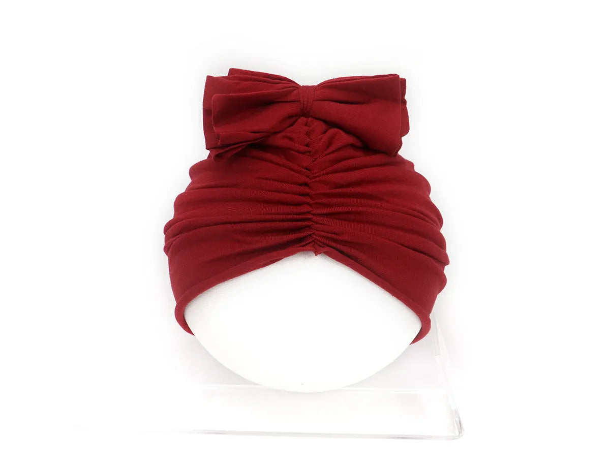Soft acrylic knitted baby hat in a solid colour, shown on a mannequin as a turban-style cap for infants 0-28 months.