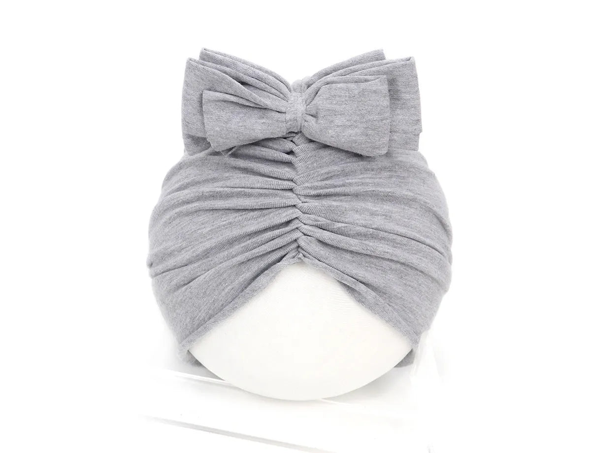 Soft acrylic knitted baby hat in a solid colour, shown on a mannequin as a turban-style cap for infants 0-28 months.