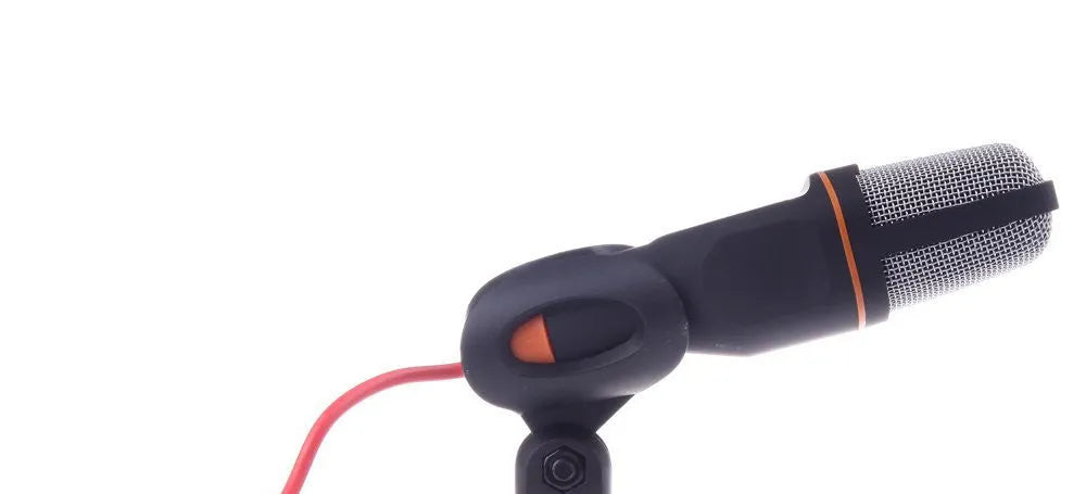 Black wired PC microphone with separate metal clip holder on a desk next to a computer.