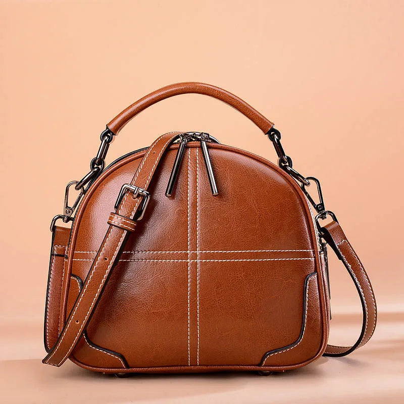 Round leather women's handbag with double soft handles and zipper closure in wine red colour