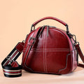 Round leather women's handbag with double soft handles and zipper closure in wine red colour