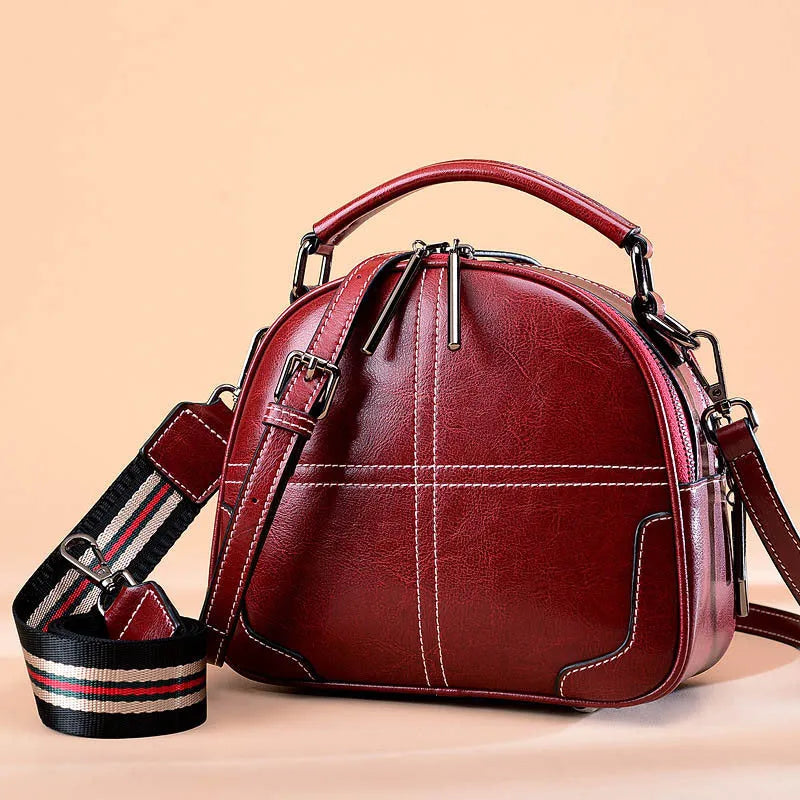 Round leather women's handbag with double soft handles and zipper closure in wine red colour