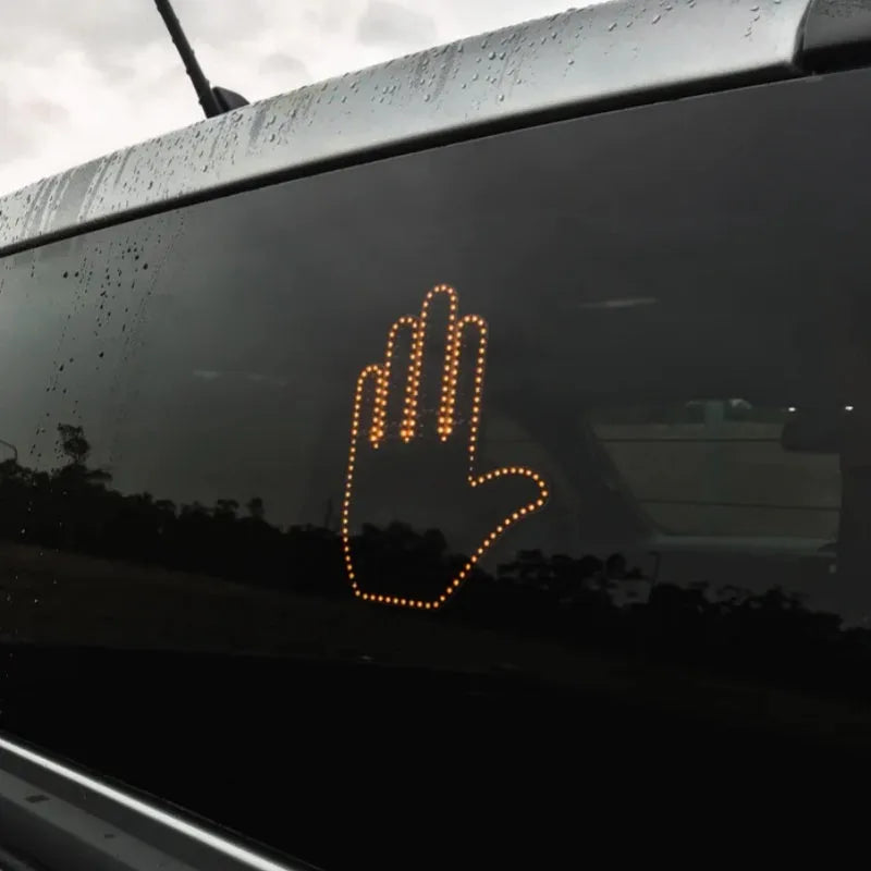 Black plastic LED gesture car light with amber LEDs showing a hand gesture, remote control, and 3M tape for mounting.