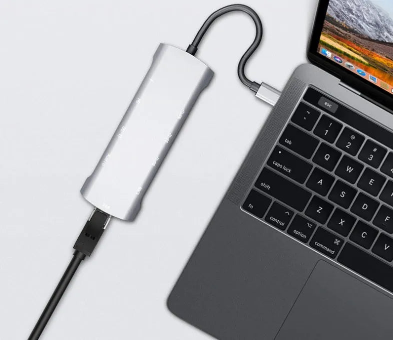 Grey aluminium USB-C docking station with HDMI, VGA, USB, and charging ports on a desk.