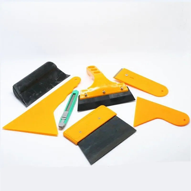 Seven-piece automotive film tool set with scrapers, knives, and a pressing block on a work surface.