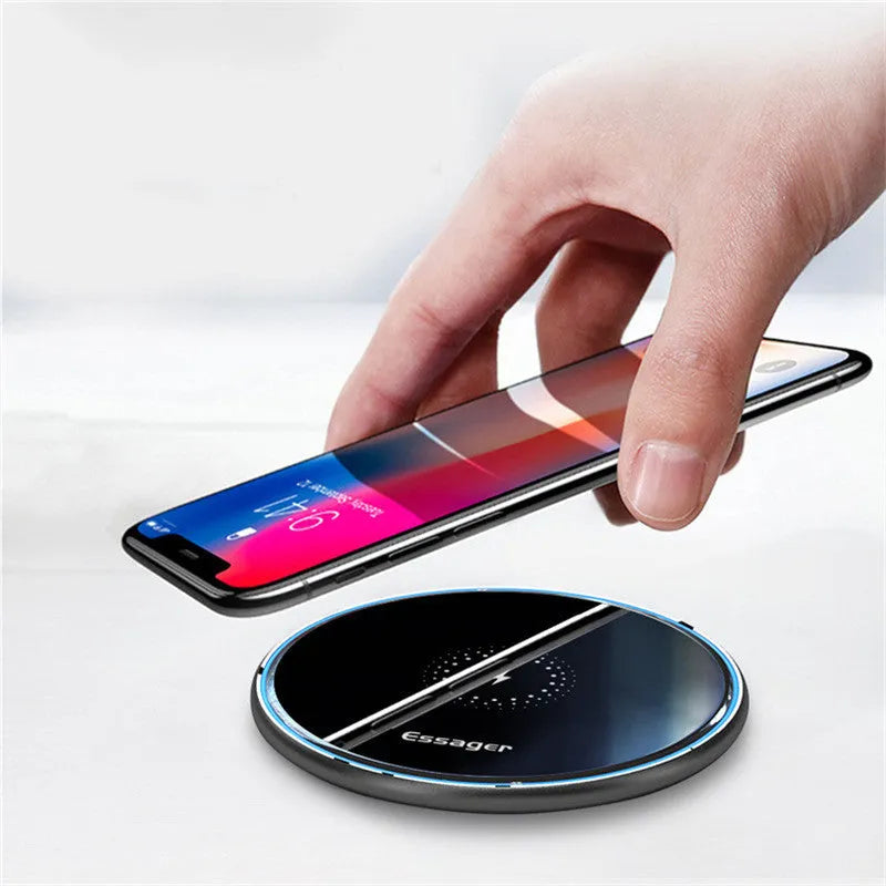 Black 15W fast wireless charging pad on a wooden desk next to a smartphone.