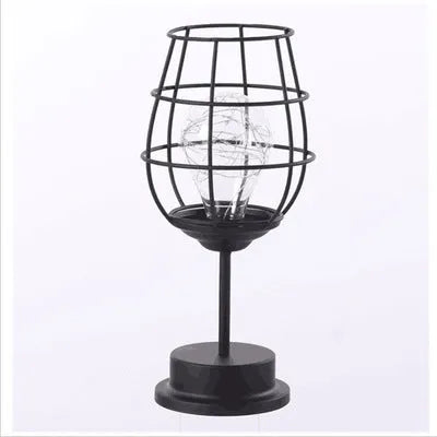 Minimalist hollow iron table lamp in red wine glass style on a wooden desk.
