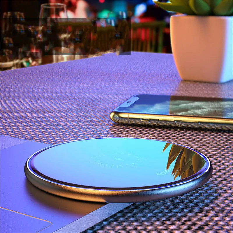 Black 15W fast wireless charging pad on a wooden desk next to a smartphone.