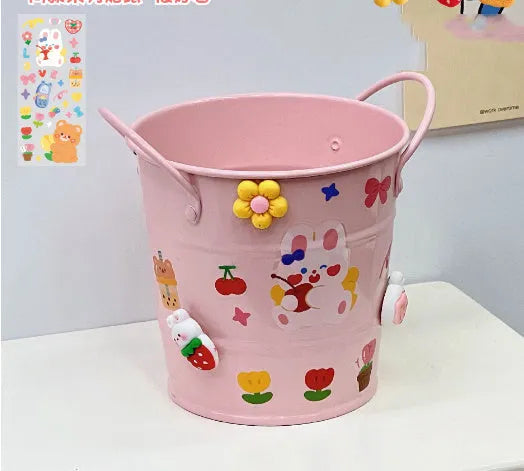 Round metal pen holder in a choice of colours including pink, green, red, white and yellow on a desk.