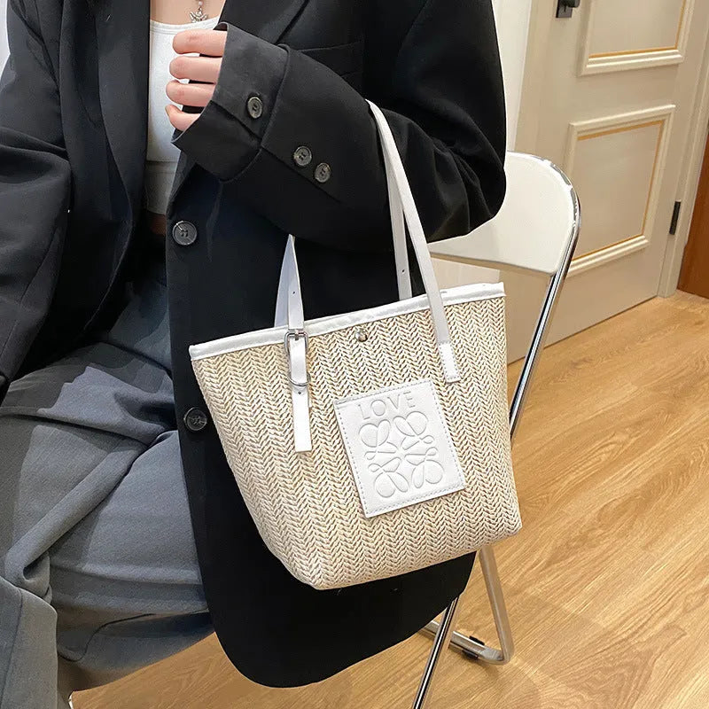 Women's straw woven shoulder bag with PU trim showing tapered shape and sewn thread details