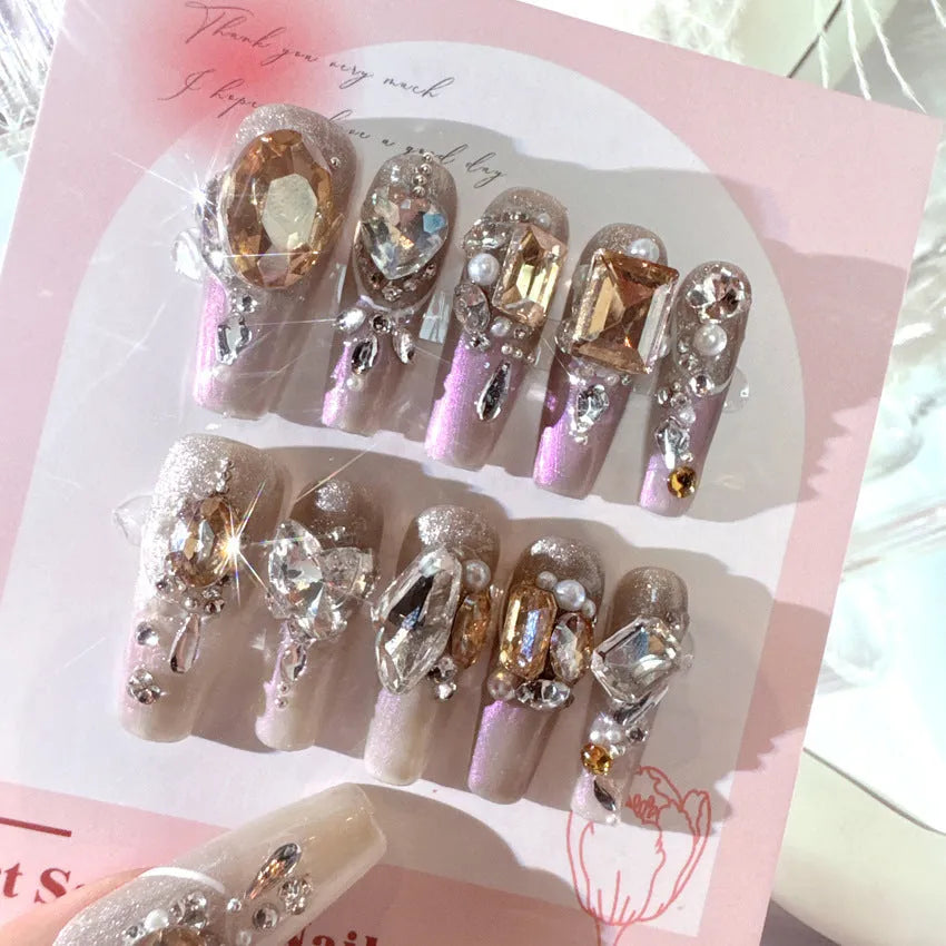 Ten false nail patches with rhinestones on a card, next to jelly adhesive and manicure tools.